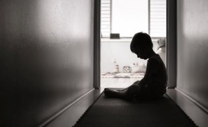 Child sitting in darkened hallway with head down. Adobe